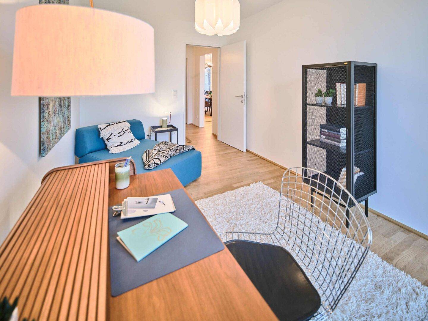 Modernes Büro mit Schreibtisch, blauem Sofa und hellem Teppich.