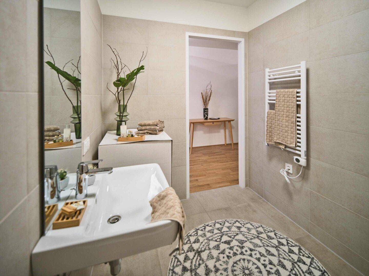 Modernes Badezimmer mit hellen Fliesen, Waschbecken und beheiztem Handtuchhalter.