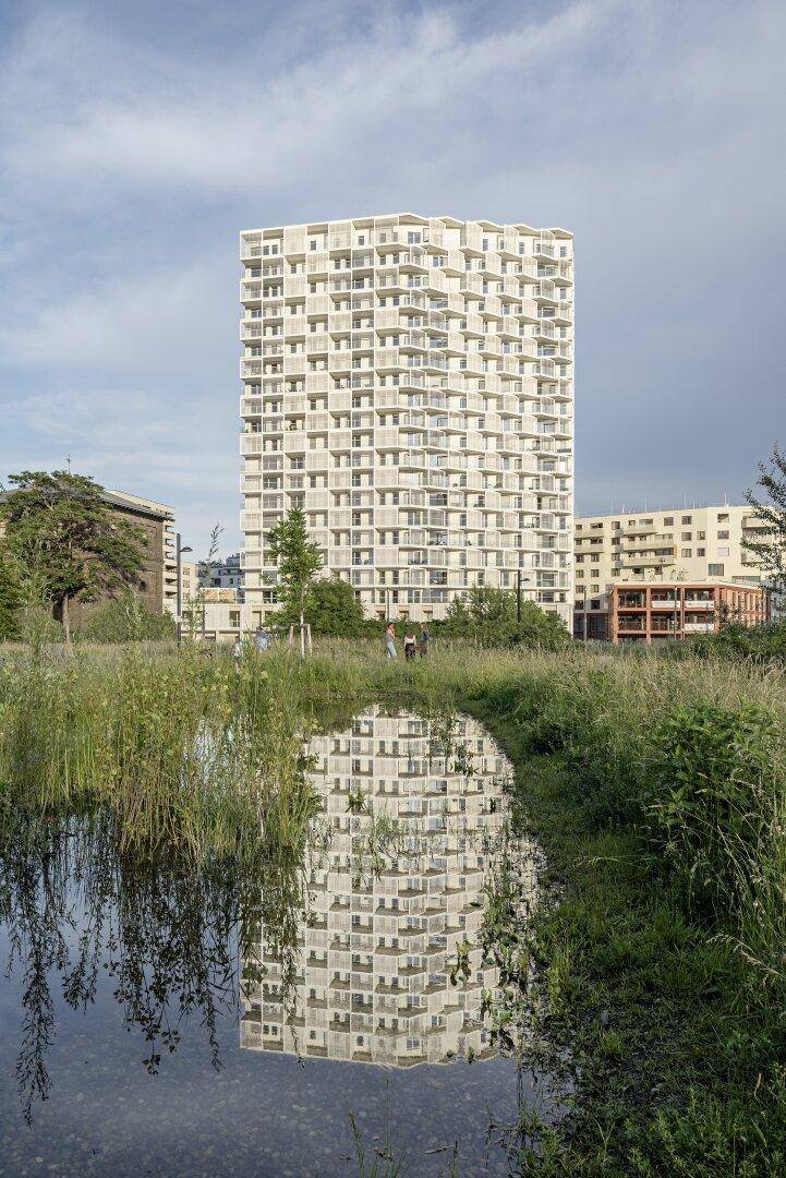 Hohes Wohngebäude spiegelt sich in einem Teich, umgeben von üppiger Vegetation.