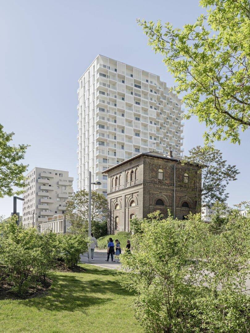 Moderne Wohngebäude und ein historisches Backsteingebäude in einer grünen Parkanlage.