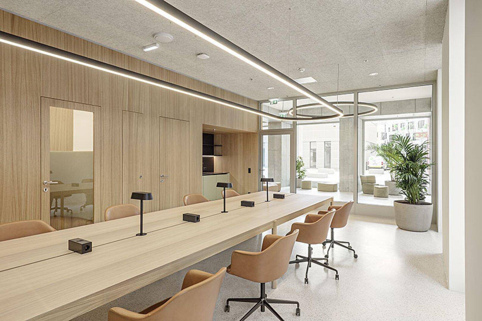 Moderner Besprechungsraum mit langem Holztisch, ergonomischen Stühlen und großen Fenstern.