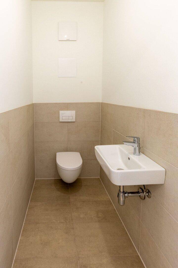 Separates Gäste-WC mit beigefarbenen Fliesen, wandhängendem WC und kleinem Waschbecken.