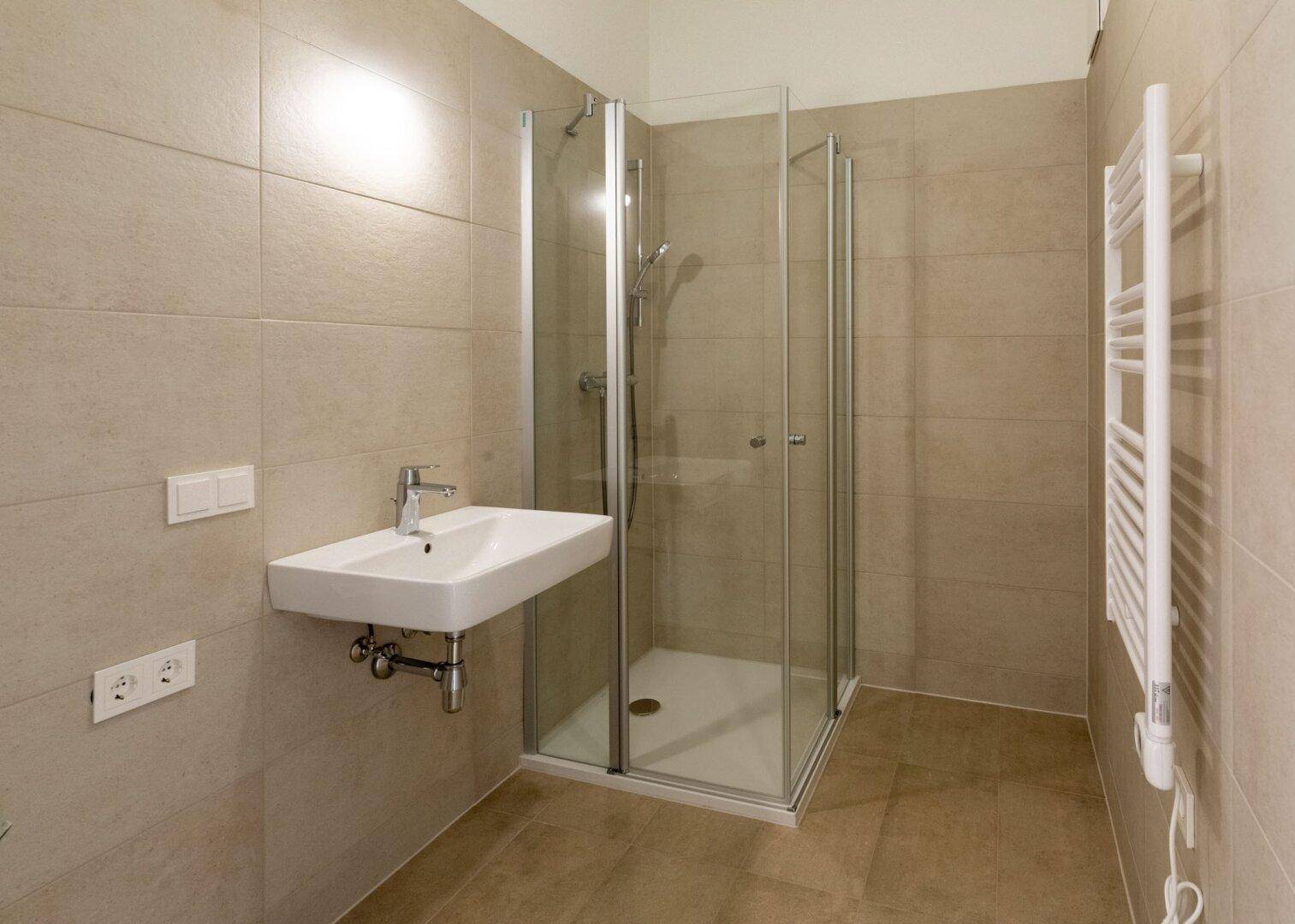 Modernes Badezimmer mit beigefarbenen Fliesen, Duschkabine und beheiztem Handtuchhalter.