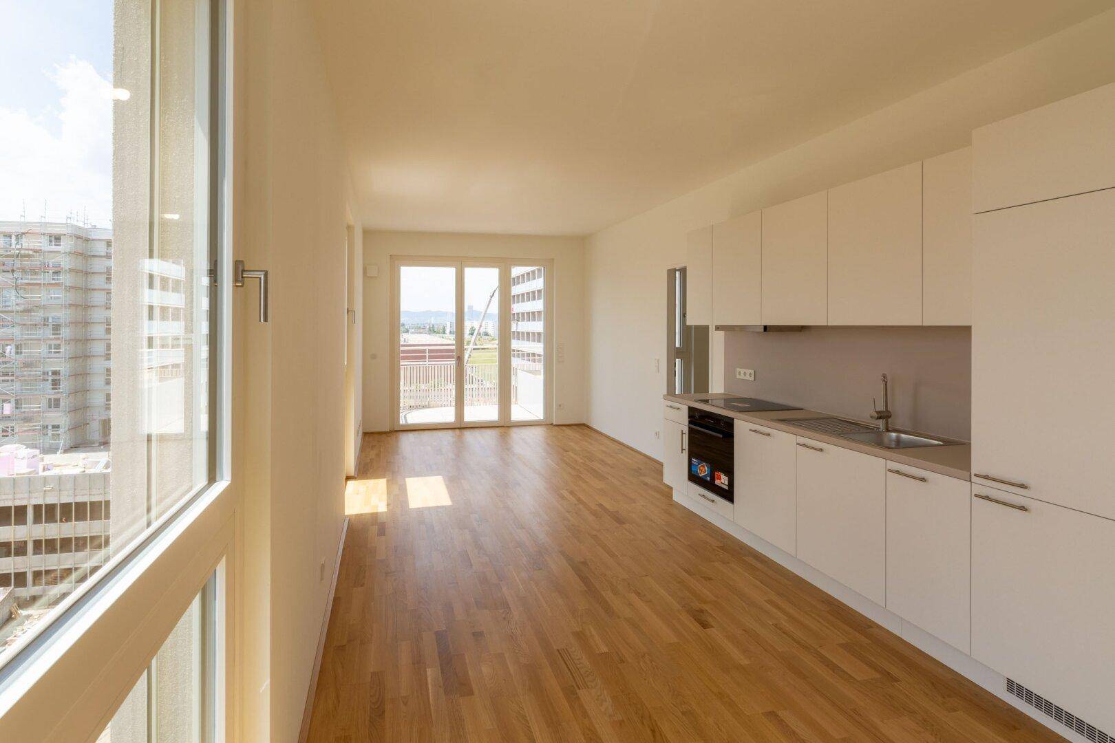 Lichtdurchfluteter Wohnbereich mit integrierter Küche, Holzboden und Zugang zu einem Balkon.