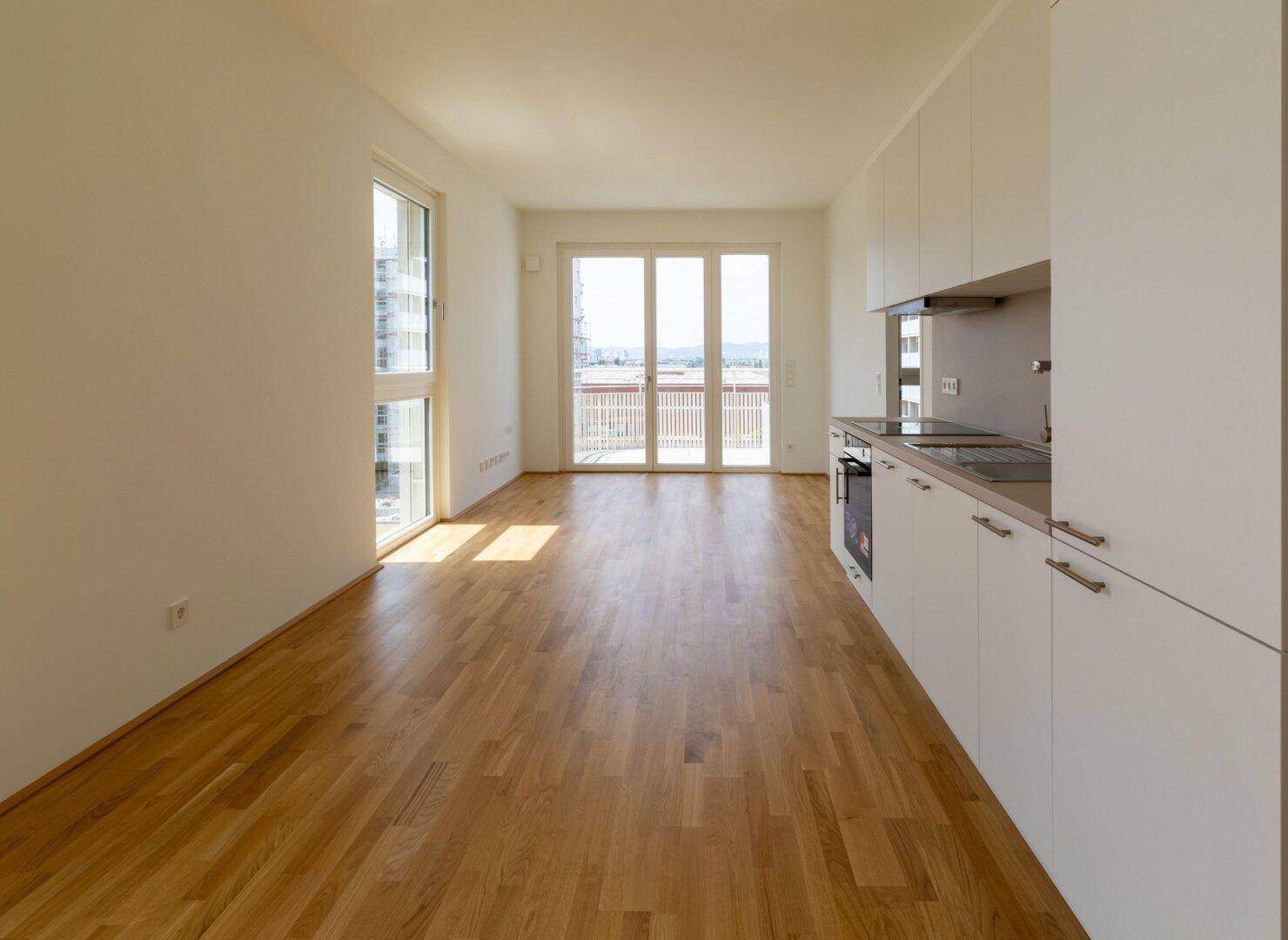 Geräumiger Wohnbereich mit Parkettboden, offener Küche und direktem Zugang zum Balkon.