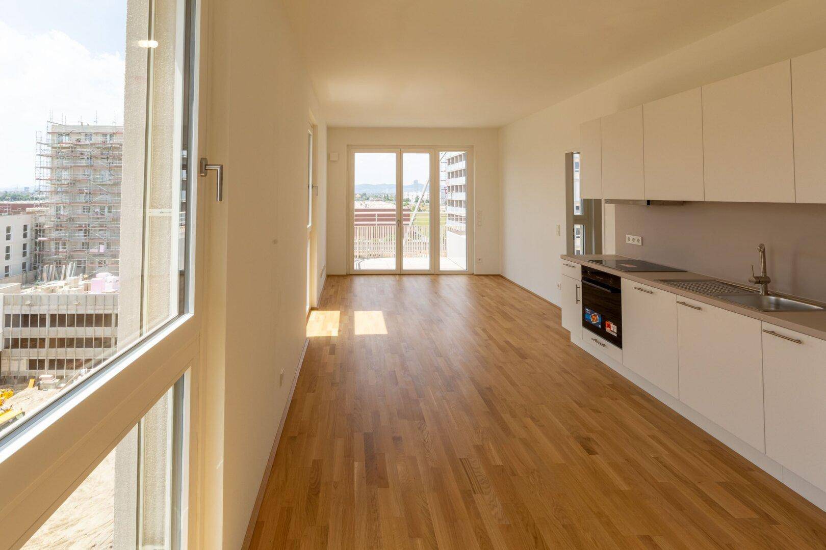 Heller Wohnbereich mit offener Küche, Parkettboden und großen Fenstern mit Blick auf die Umgebung.