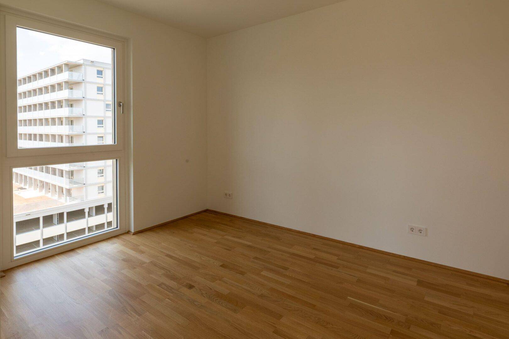 Helles Schlafzimmer mit Parkettboden, weißen Wänden und einem großen Fenster mit Stadtblick.