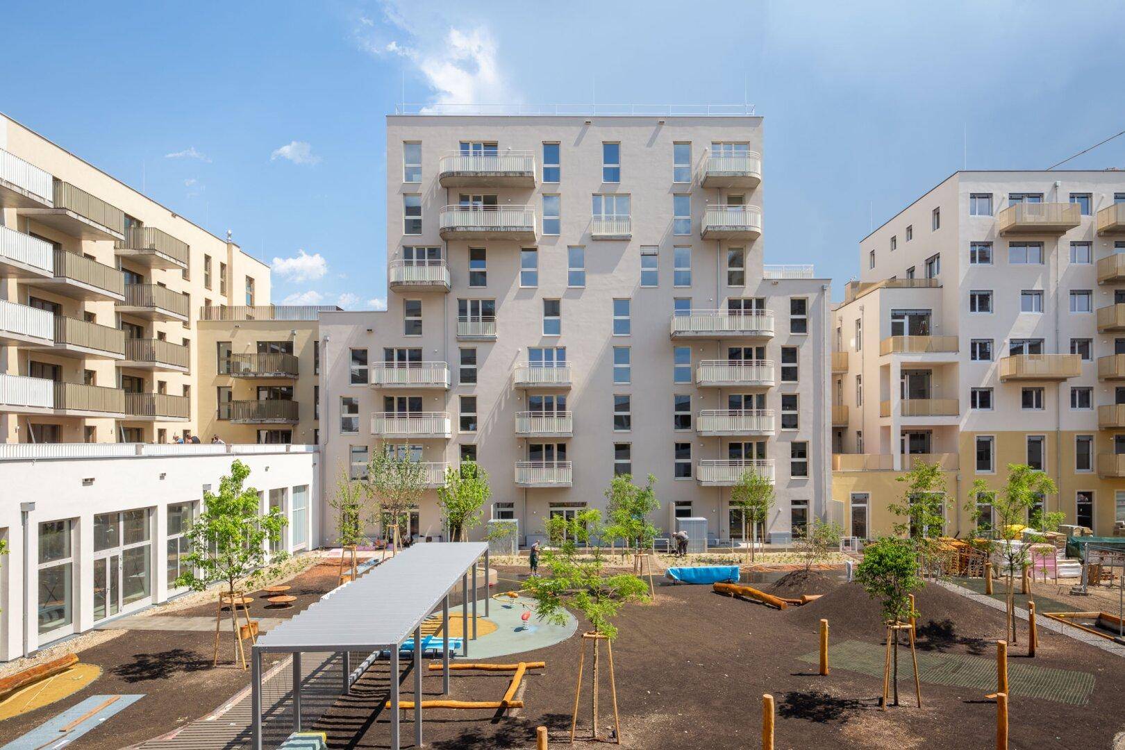 Moderner Wohnkomplex mit mehreren Gebäuden und einem zentralen Spielplatz im Innenhof.