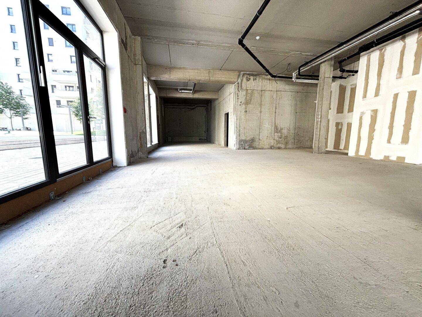 Geräumiger, unfertiger Gewerberaum mit Betonwänden und -boden, bereit für den Innenausbau.