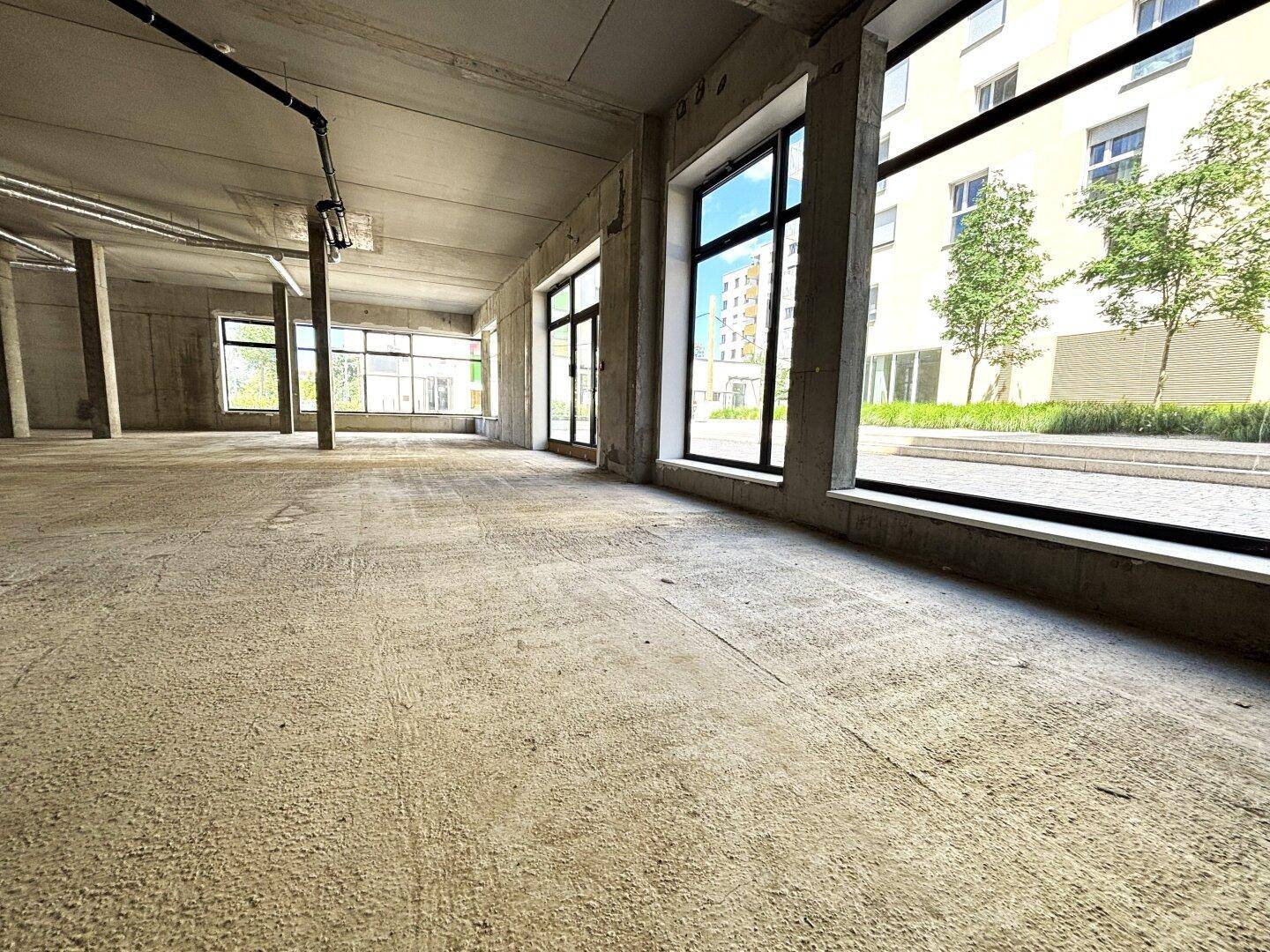 Weitläufiger, unfertiger Gewerberaum mit großen Fensterfronten und Blick auf die umliegenden Gebäude.