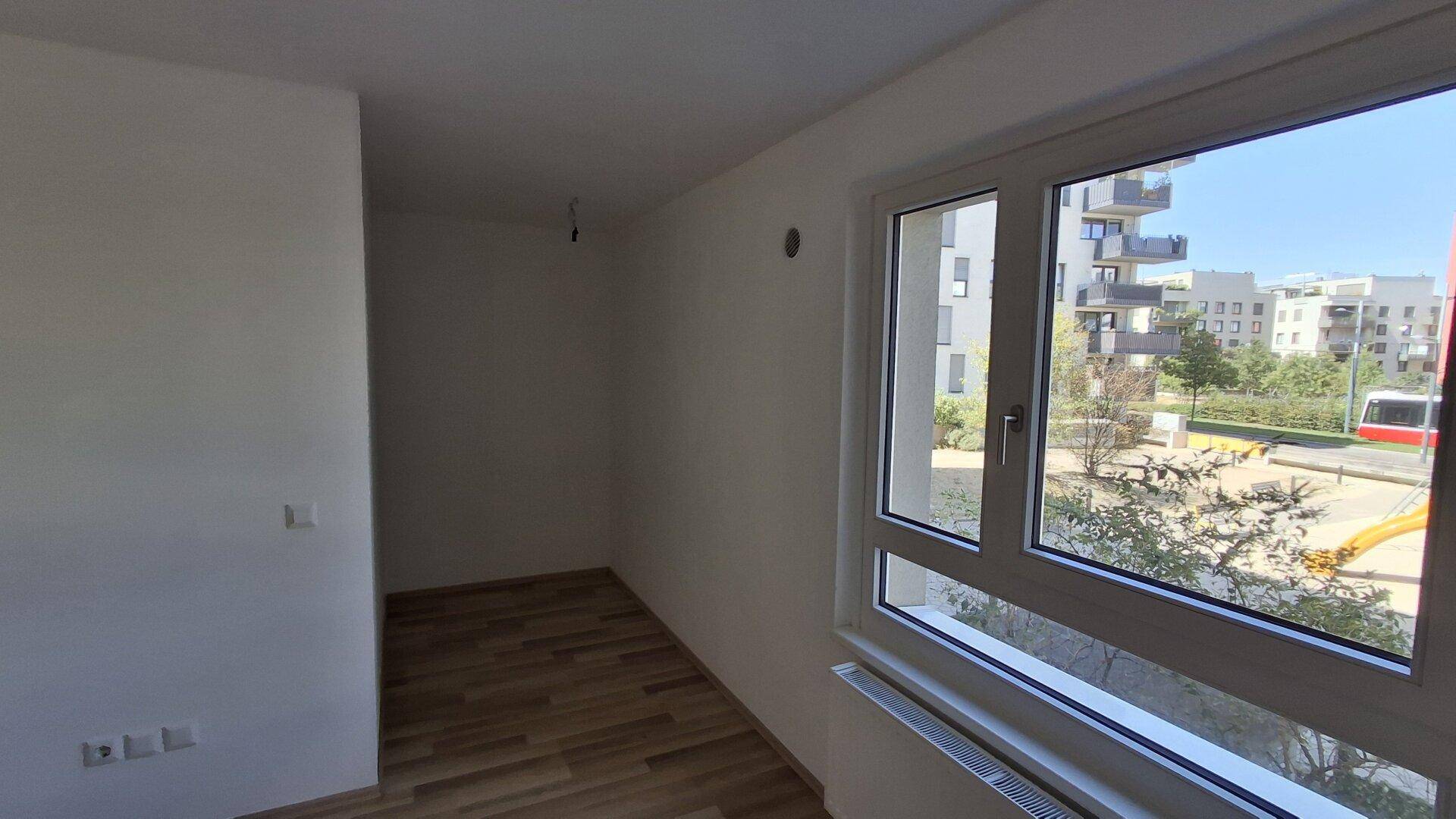 Helles Zimmer mit Laminatboden und großem Fenster, das viel Tageslicht hereinlässt.