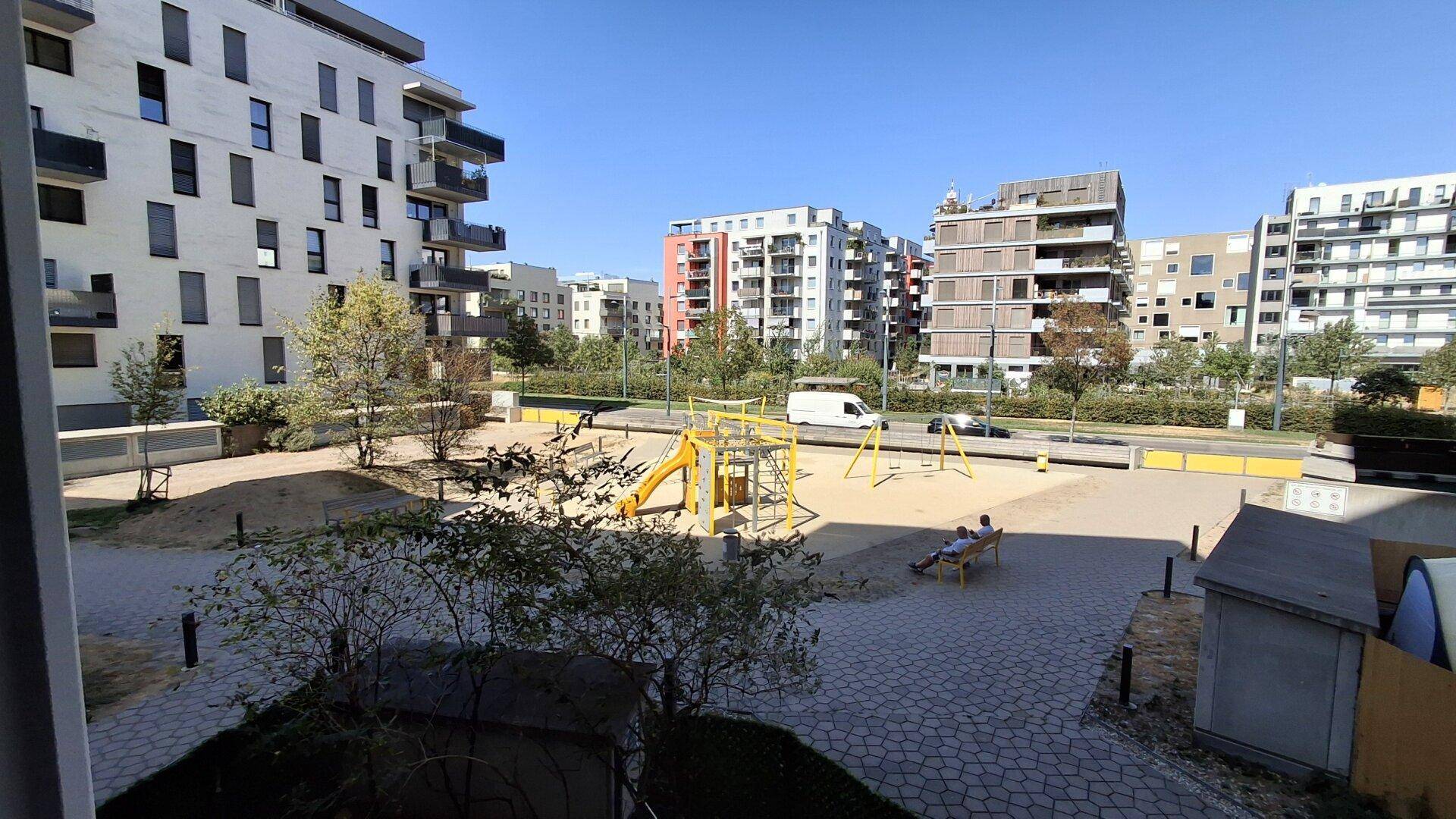 Außenbereich mit Spielplatz und Sitzgelegenheiten, umgeben von modernen Wohngebäuden.