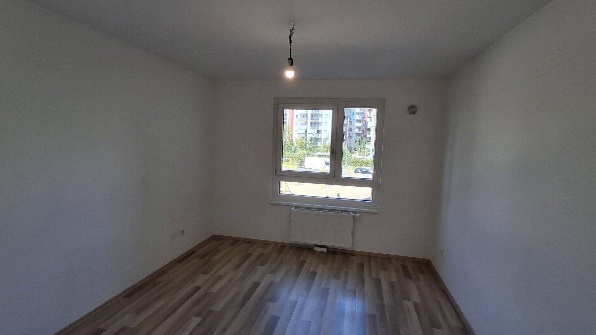 Unmöbliertes Zimmer mit Laminatboden und einem Fenster, das einen Blick auf die Umgebung bietet.