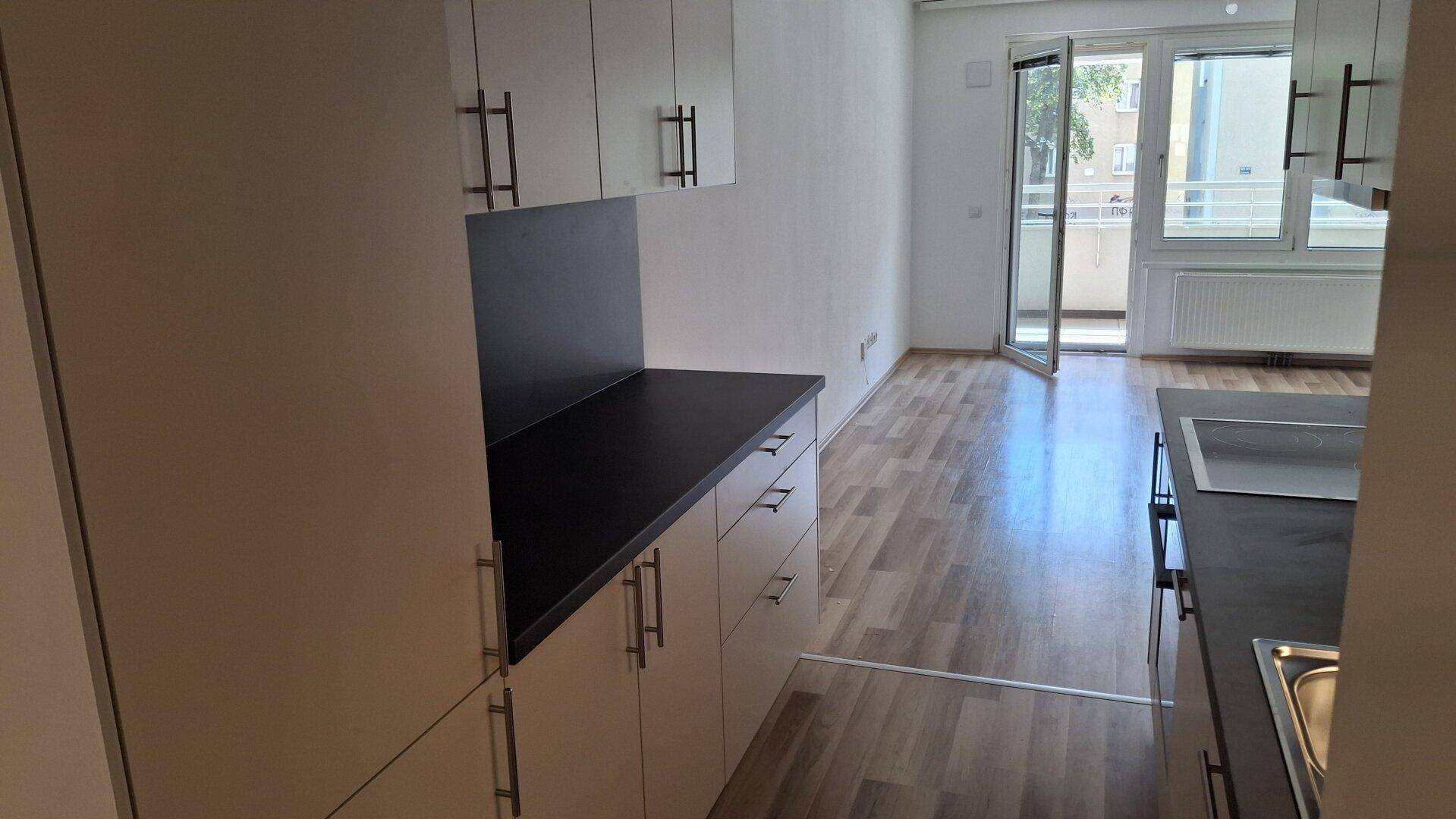 Küchenbereich mit hellen Schränken und dunkler Arbeitsplatte, offen zum angrenzenden Wohnraum.