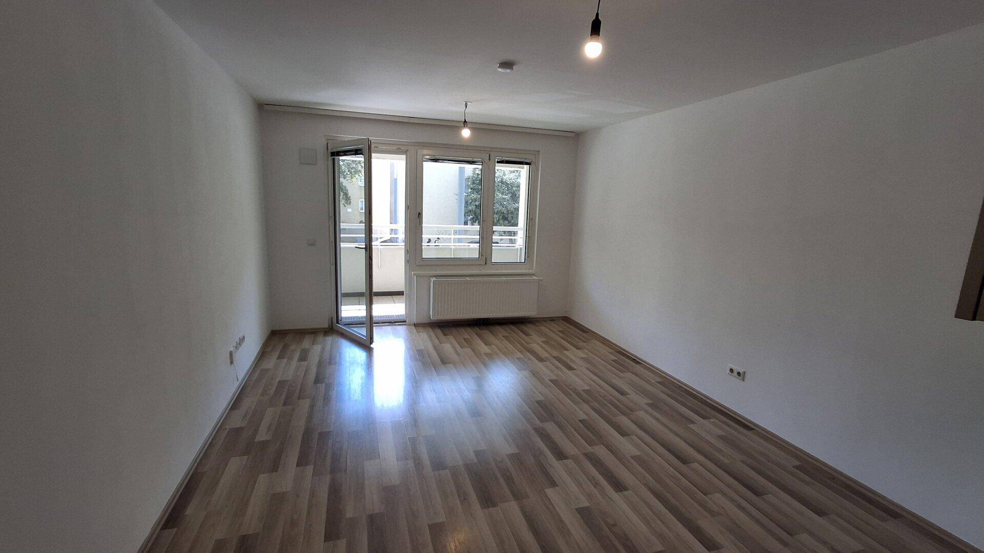 Geräumiges Wohnzimmer mit Laminatboden und Zugang zu einem Balkon, der viel Licht hereinlässt.
