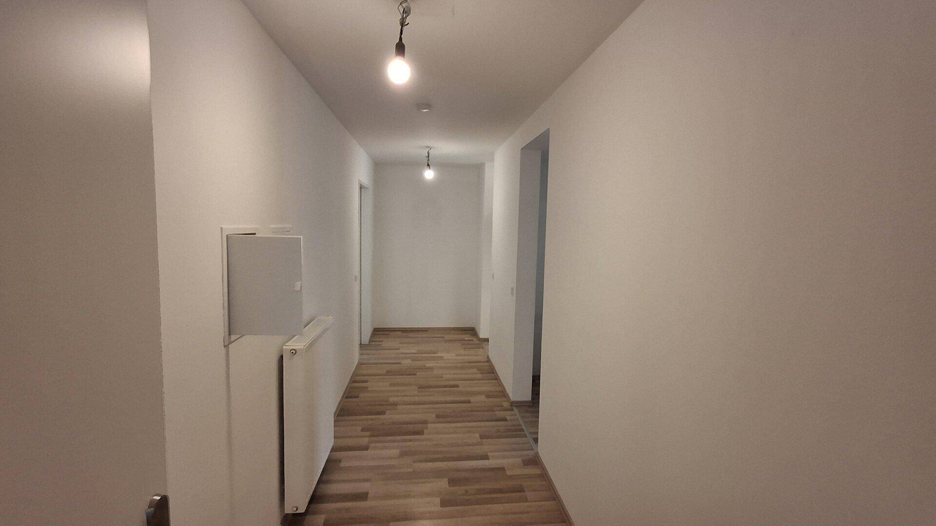 Heller Flur mit modernem Laminatboden und weißen Wänden, der zu weiteren Räumen führt.