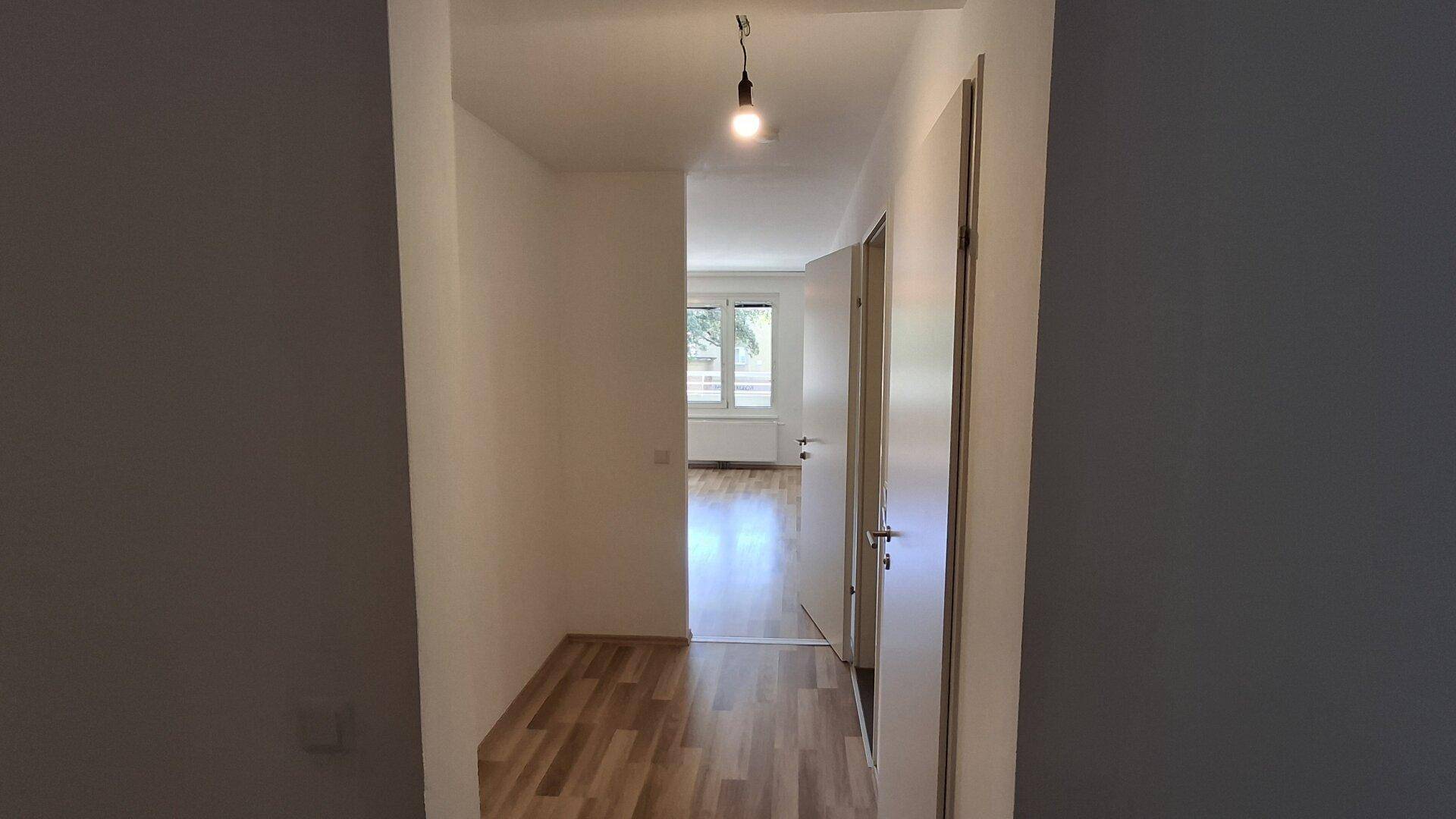 Langer, heller Flur mit Laminatboden, der den Zugang zu verschiedenen Zimmern ermöglicht.