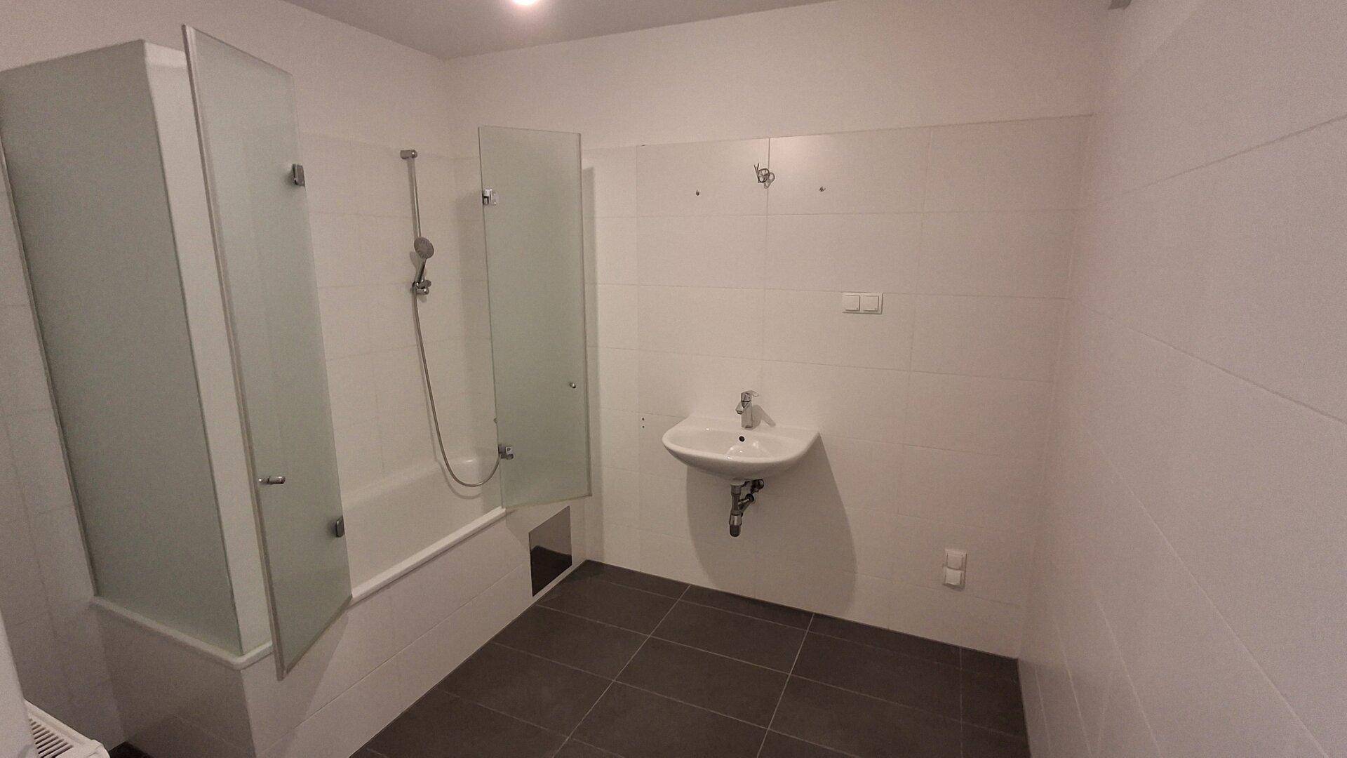 Modernes Badezimmer mit Badewanne, Duschabtrennung und Waschbecken, in hellen Fliesen gehalten.