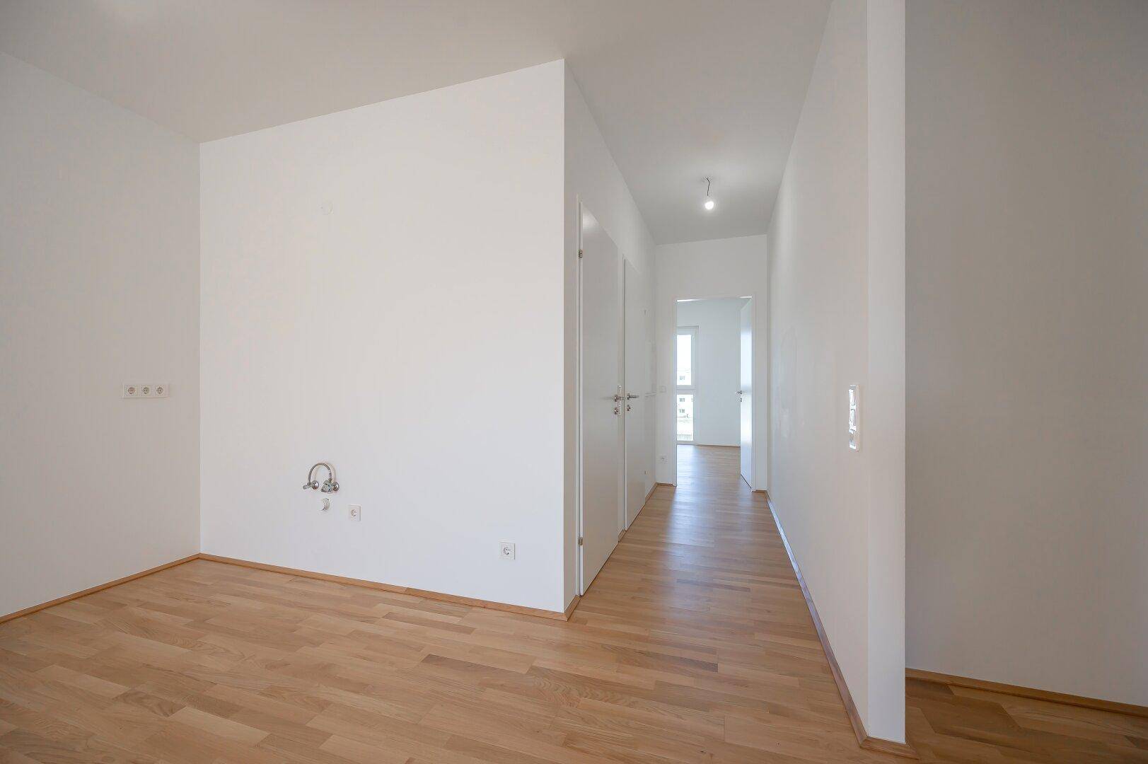 Langer Flur mit Holzboden und Anschlüssen für eine Waschmaschine oder Spüle.