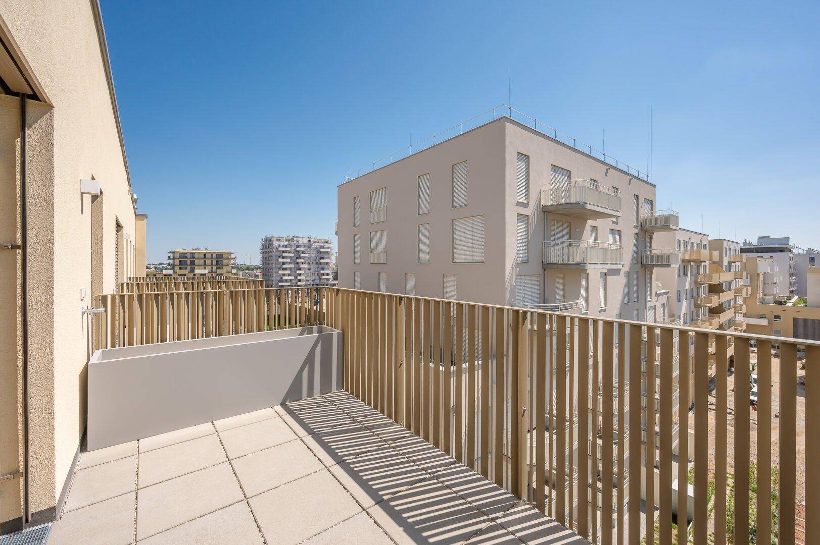 Geräumige Terrasse mit Holzzaun und Blick auf die umliegenden modernen Gebäude.