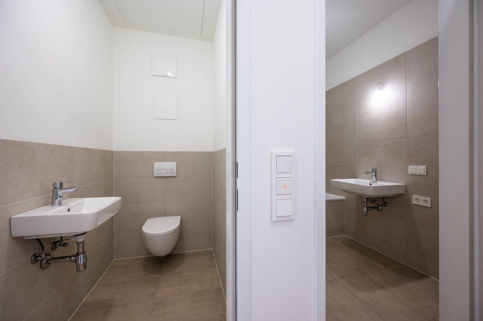 Modernes Gäste-WC mit Wand-WC und Waschbecken, daneben ein weiteres Badezimmer.