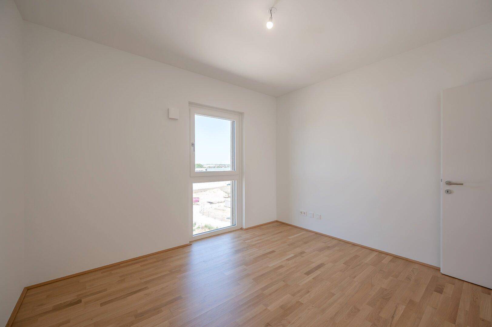 Leeres Zimmer mit Holzboden und großem Fenster, das einen weiten Blick bietet.
