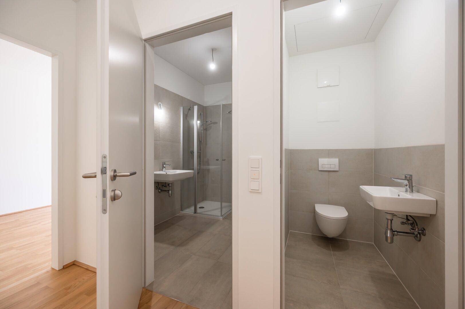 Blick in ein Badezimmer mit Dusche und ein separates WC mit wandhängender Toilette.