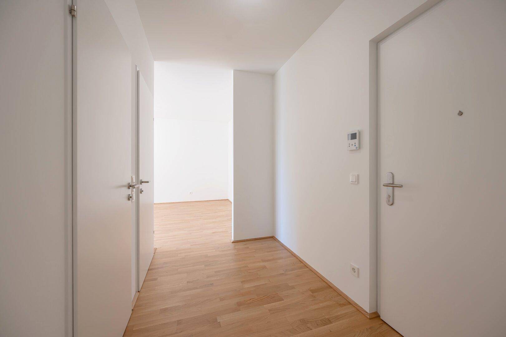 Heller Eingangsbereich mit Parkettboden, weißen Türen und einer Gegensprechanlage.