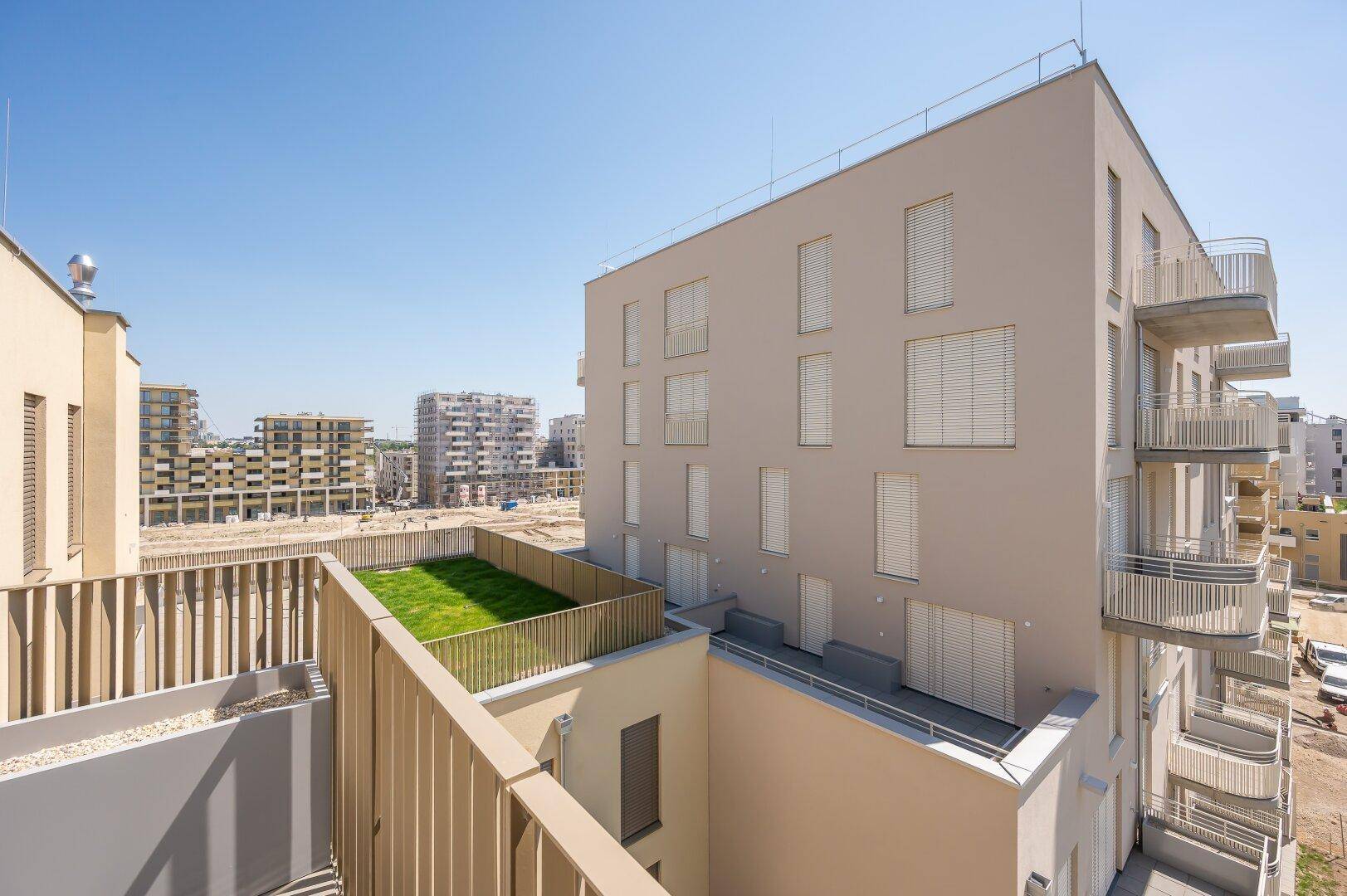 Blick von einem Balkon auf eine begrünte Dachfläche und weitere moderne Wohngebäude.