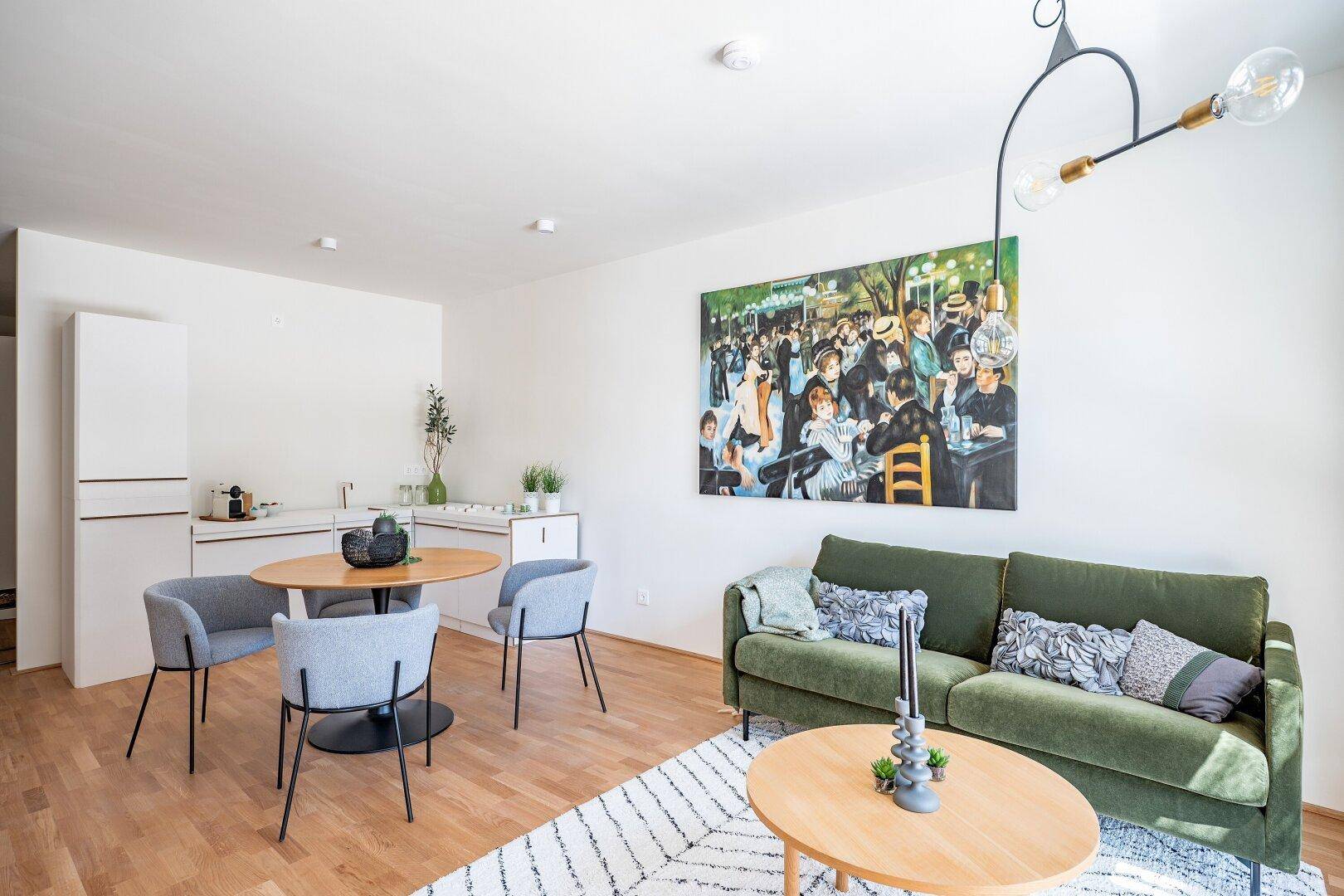 Geräumiger offener Wohn- und Essbereich mit integrierter Küchenzeile, grünem Sofa und Holzboden.