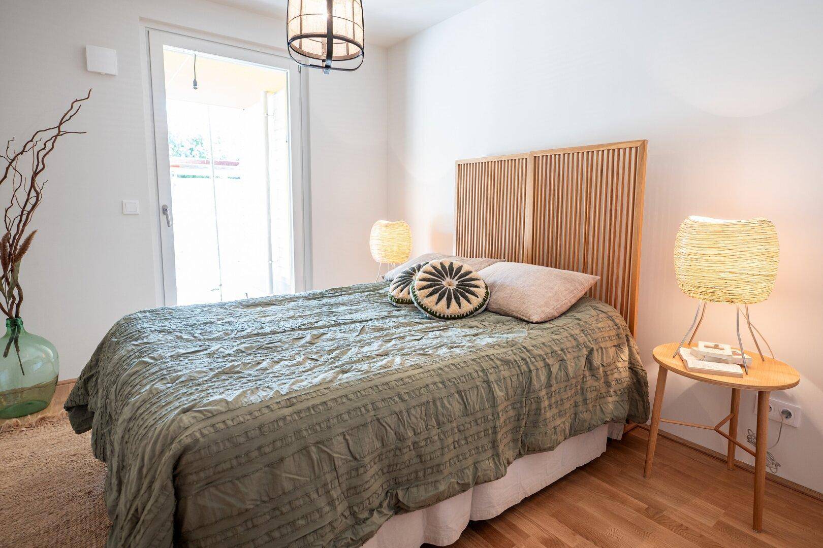 Schlafzimmer mit Holzbett, Nachttischen und direktem Zugang zu einem Außenbereich, hell und einladend.