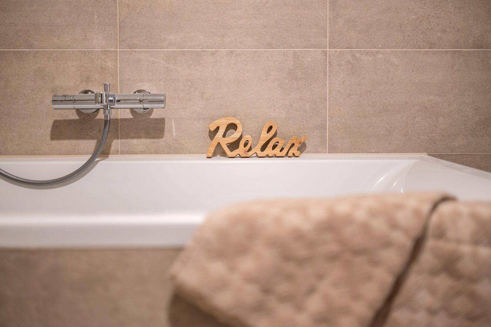 Nahaufnahme der Badewanne mit einem "Relax"-Schriftzug und einem Handtuch, das zur Entspannung einlädt.