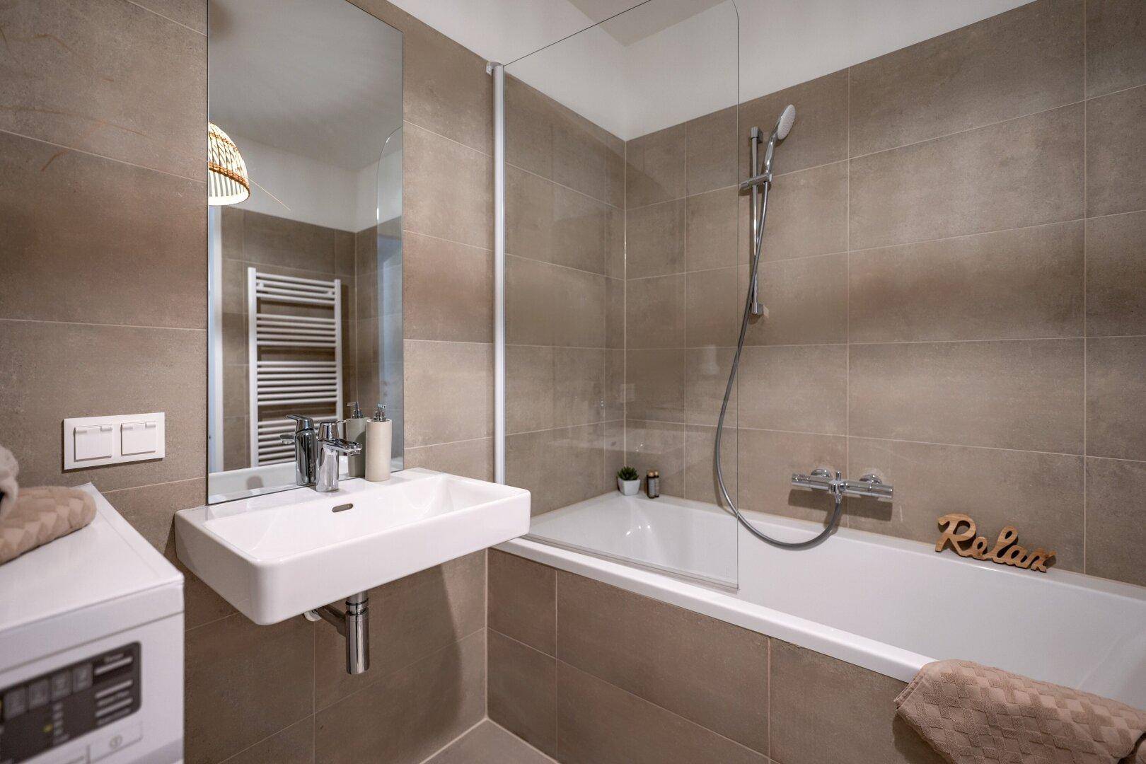 Modernes Badezimmer mit Badewanne, Duschvorrichtung, Einzelwaschbecken und beheiztem Handtuchhalter.