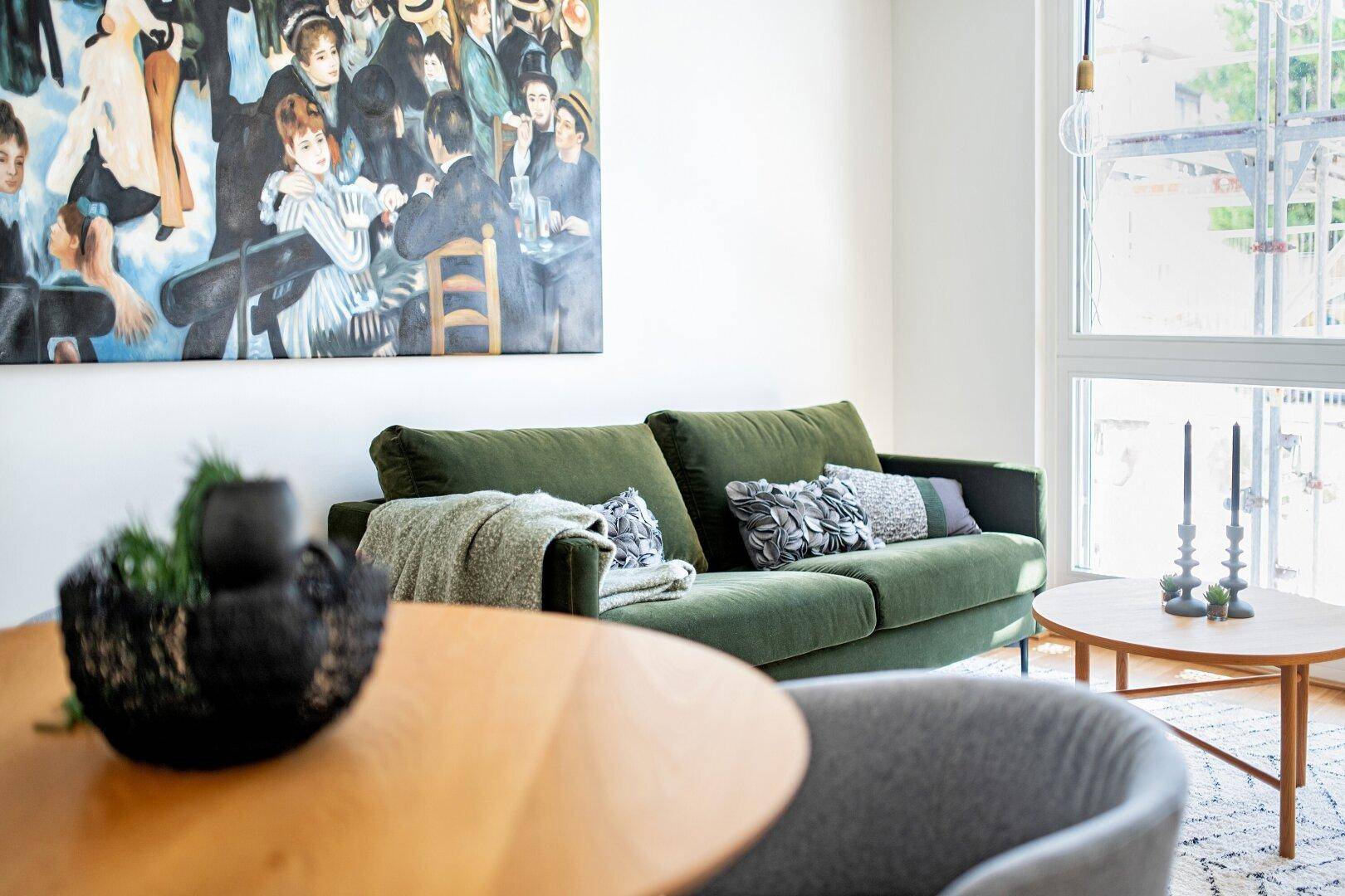 Gemütlicher Wohnbereich mit grünem Sofa, Holztisch und großem Fenster für viel Tageslicht.
