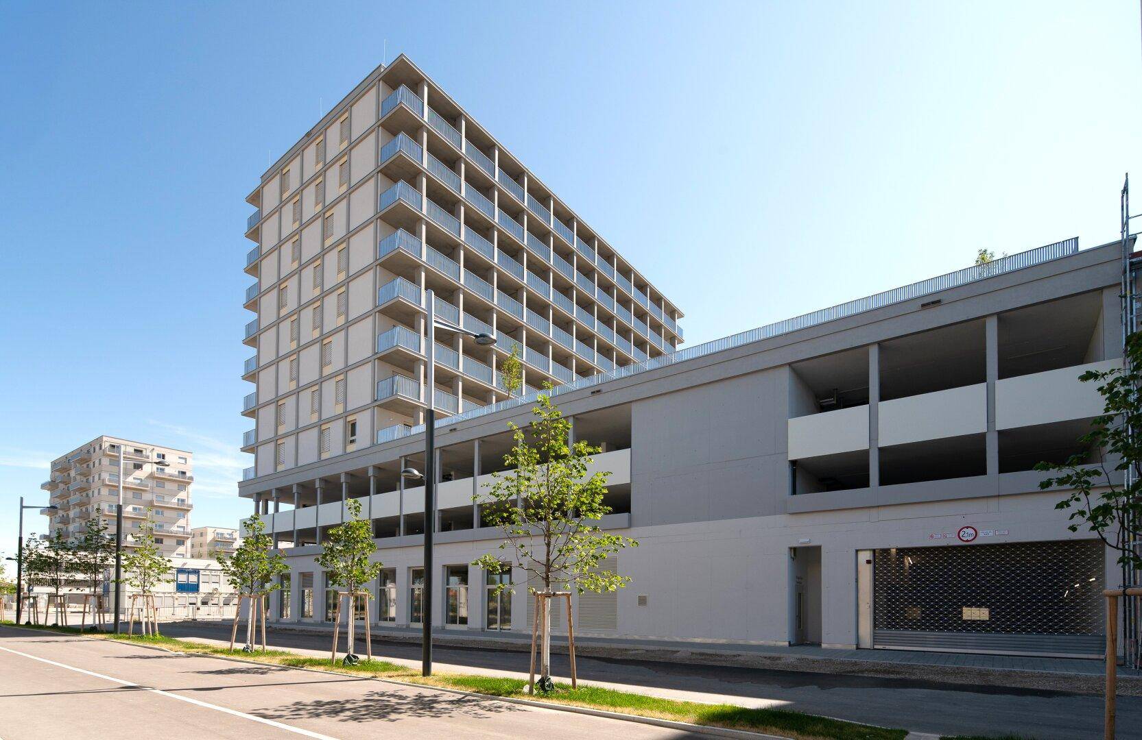 Moderne Wohnanlage von der Straße aus gesehen, mit Tiefgaragenzufahrt und Baumbepflanzung.