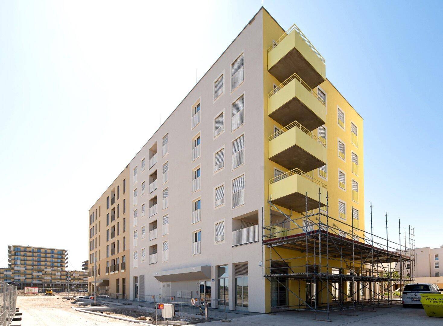 Modernes Wohngebäude mit gelben und weißen Fassaden, Balkonen und Baugerüst.