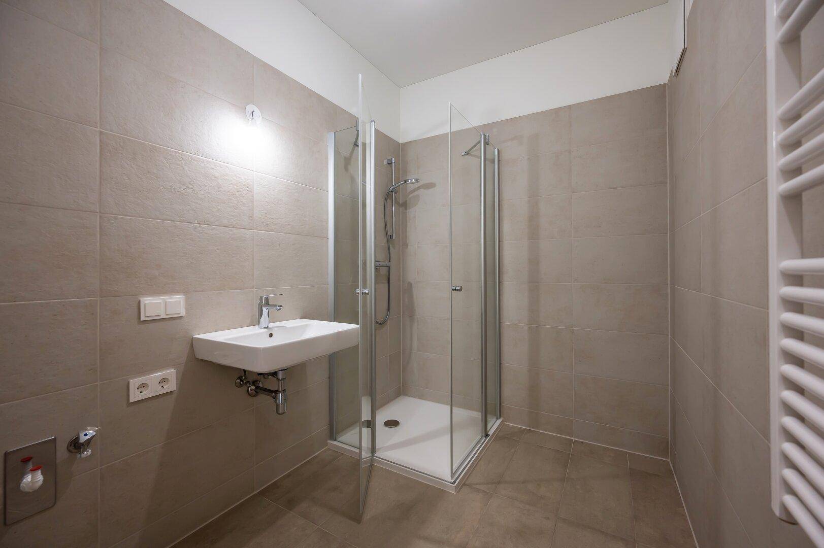 Modernes Badezimmer mit grauen Fliesen, Duschkabine und beheiztem Handtuchhalter.