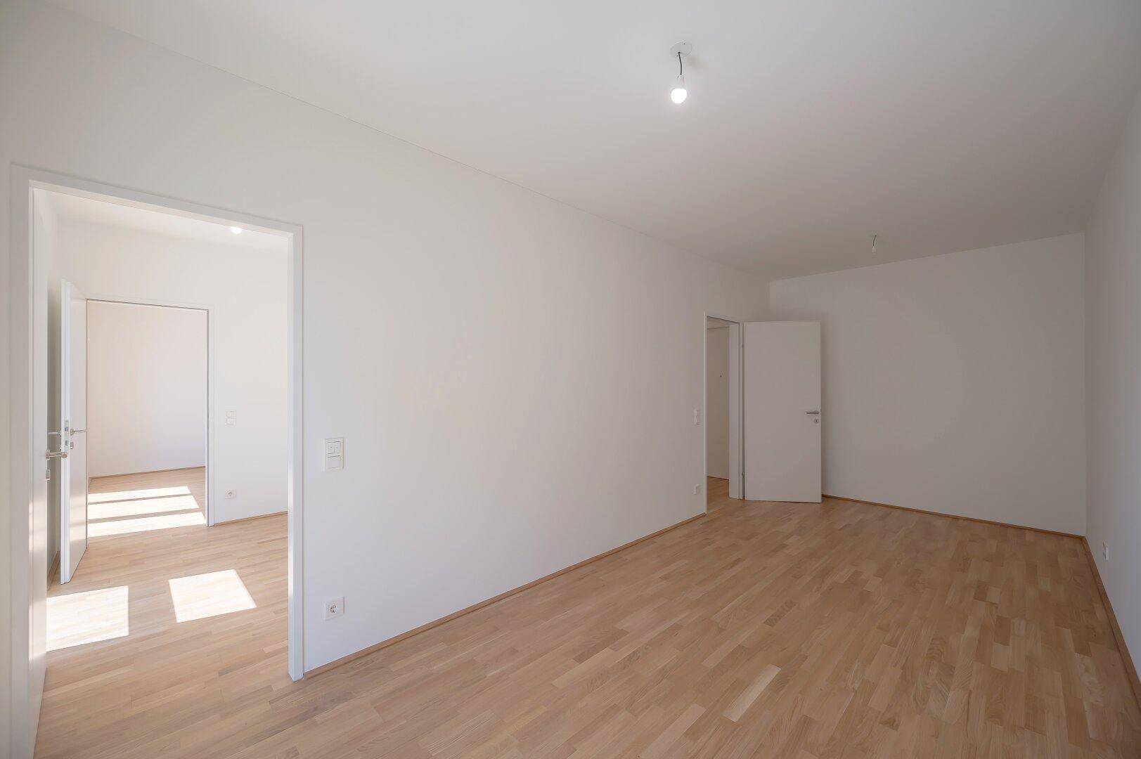 Geräumiges, leeres Zimmer mit Parkettboden und mehreren Türen, ideal für flexible Nutzung.