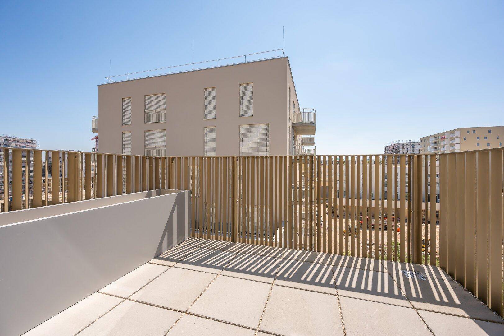 Geräumige Terrasse mit Fliesenboden und Holzlamellen als Sichtschutz in einer modernen Wohnanlage.