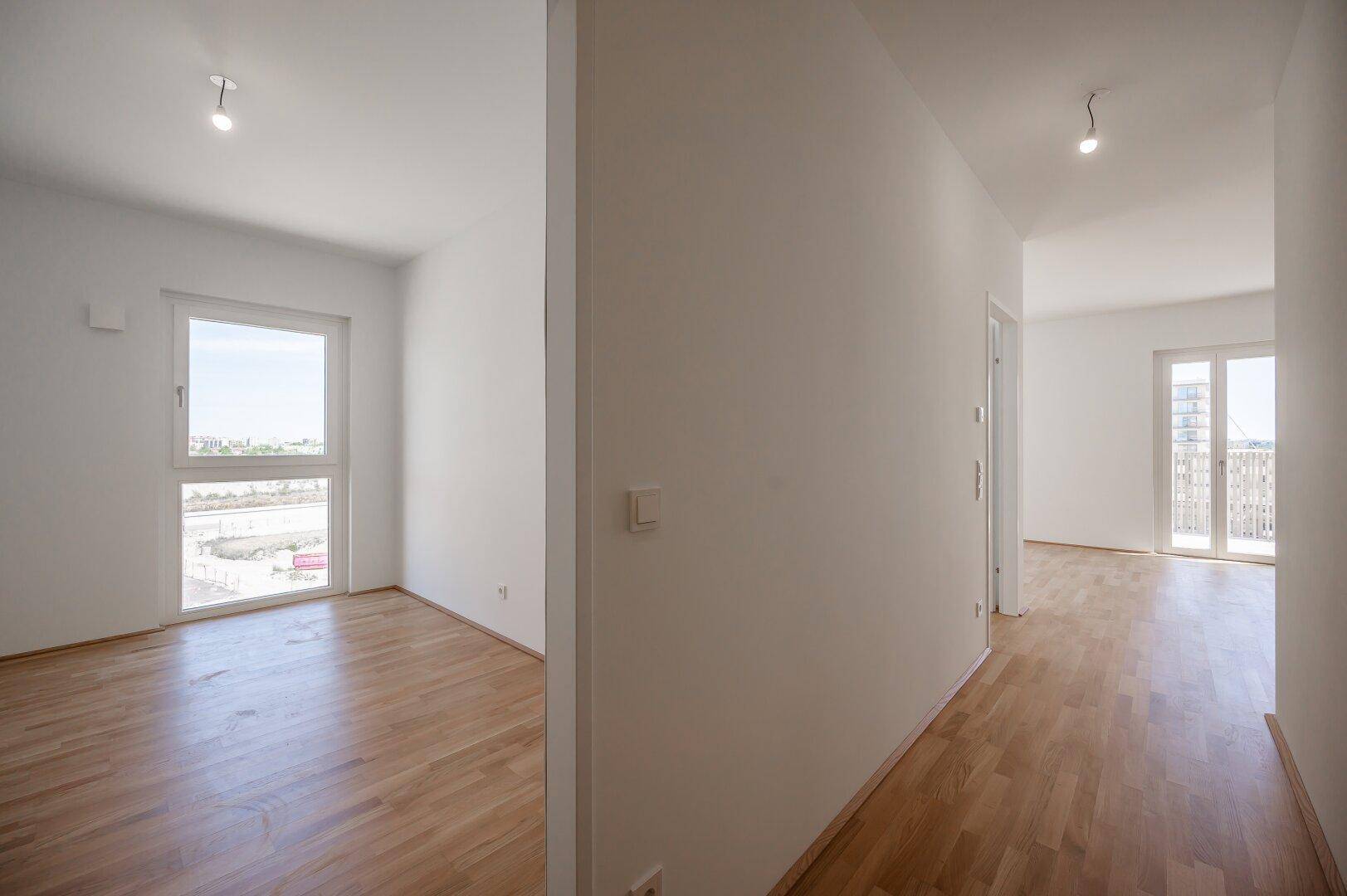 Heller Flur mit Parkettboden, der zu verschiedenen Zimmern und einem Balkon führt.