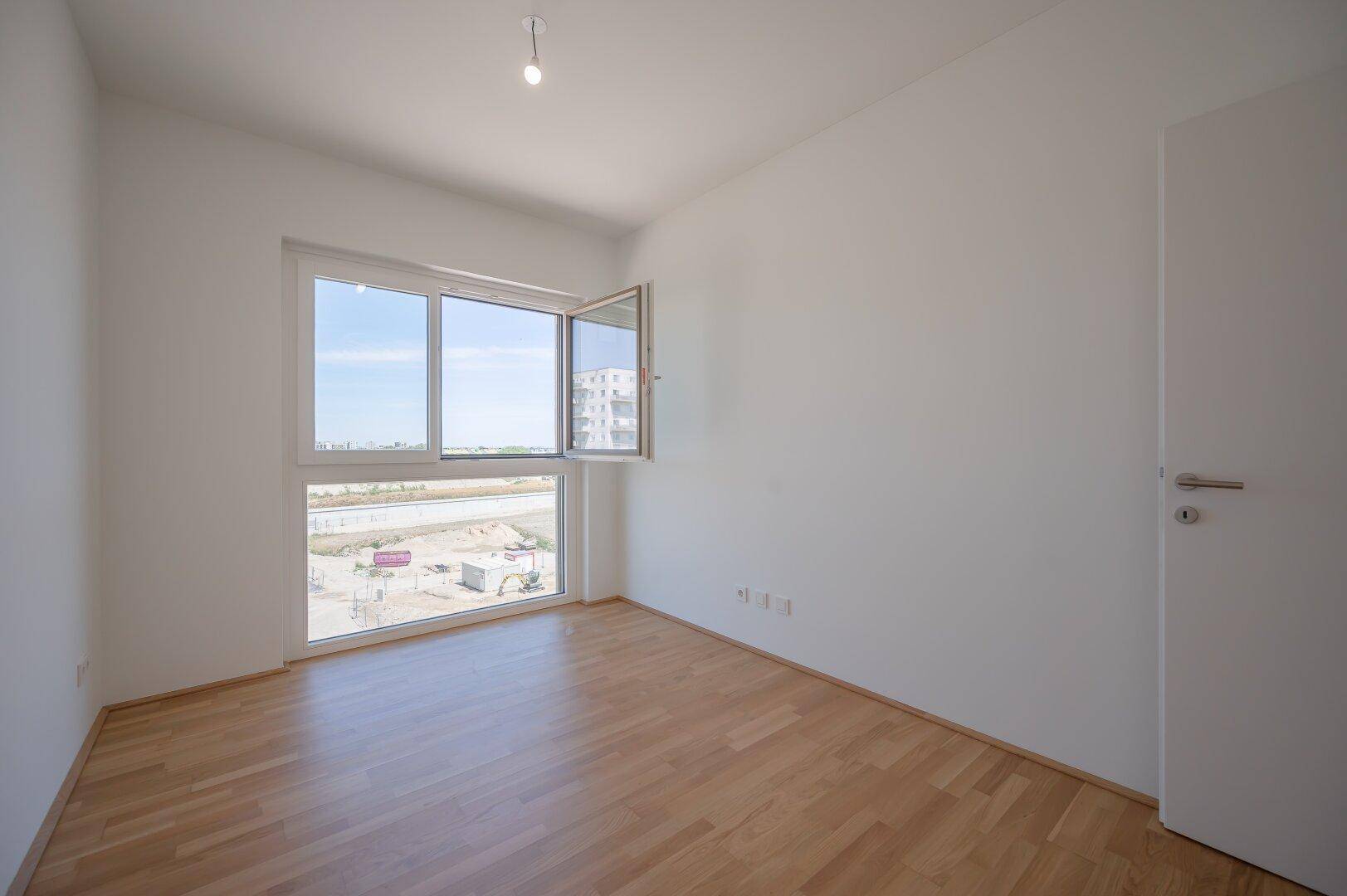 Freundliches Zimmer mit Holzparkett und großem Fenster, ideal als Schlaf- oder Arbeitszimmer.