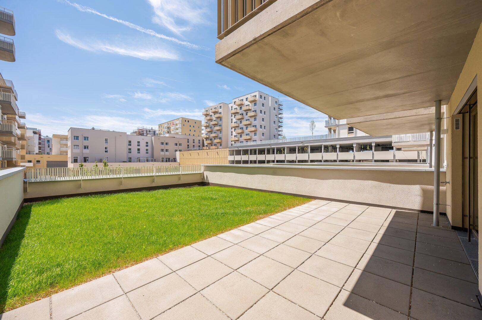 Sonnige Terrasse mit Rasenfläche und Blick auf die umliegenden Neubauten.