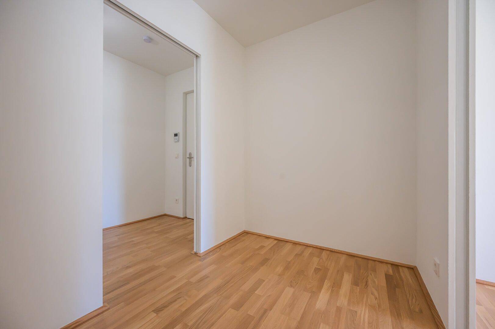 Leeres Zimmer mit Parkettboden und Schiebetür zum angrenzenden Bereich.