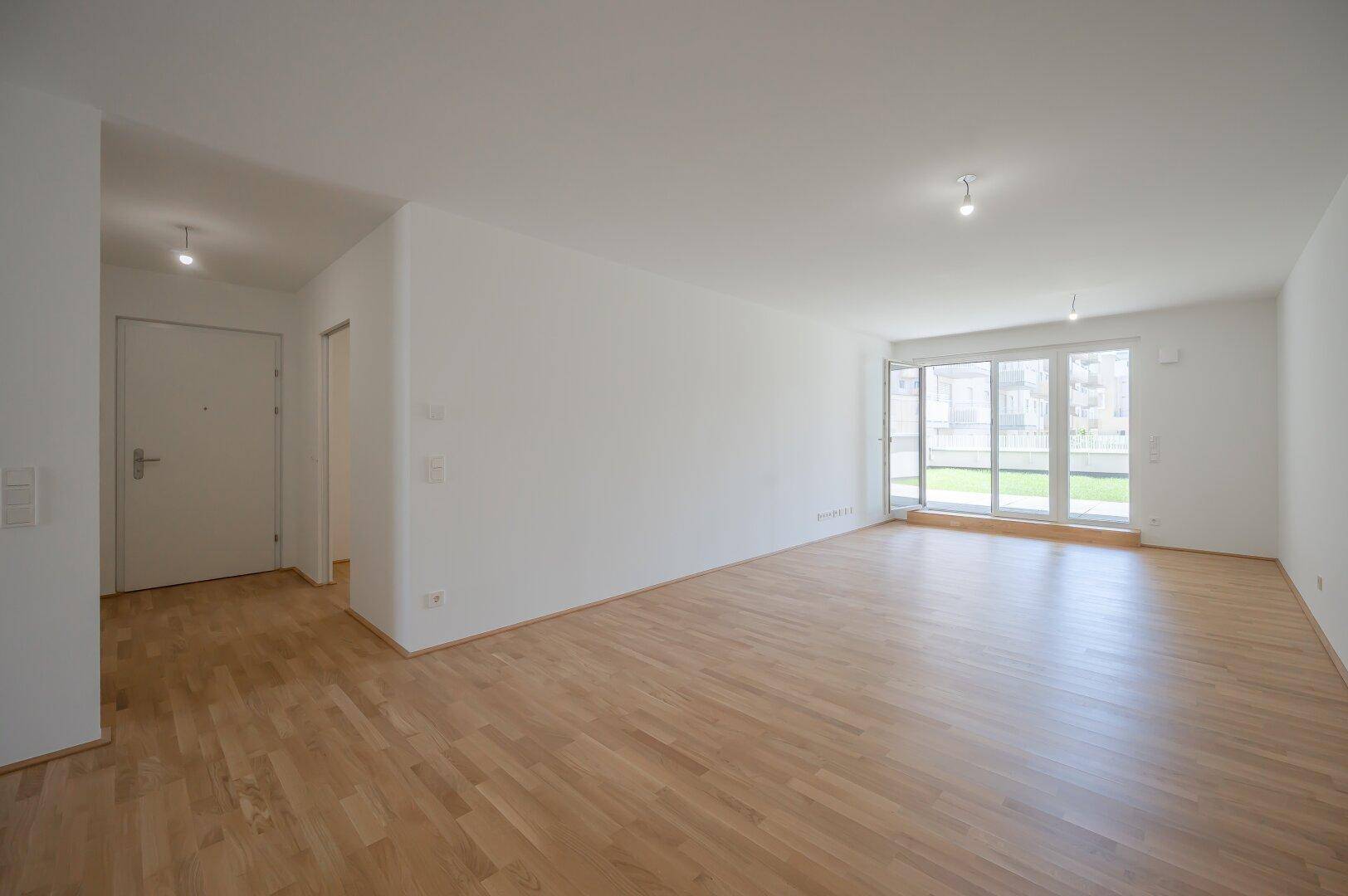 Geräumiger, heller Wohnbereich mit Parkettboden und Zugang zum Eingangsbereich.