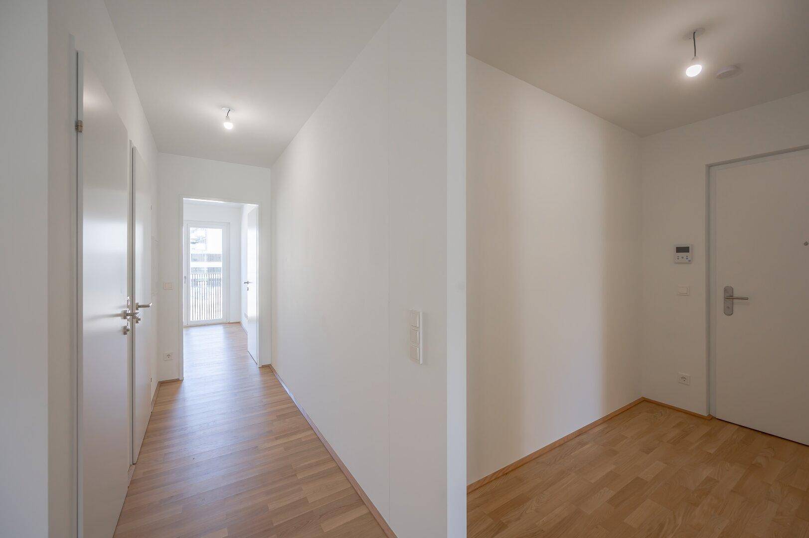 Langer, heller Flur mit Parkettboden und weißen Wänden in einem Neubau.