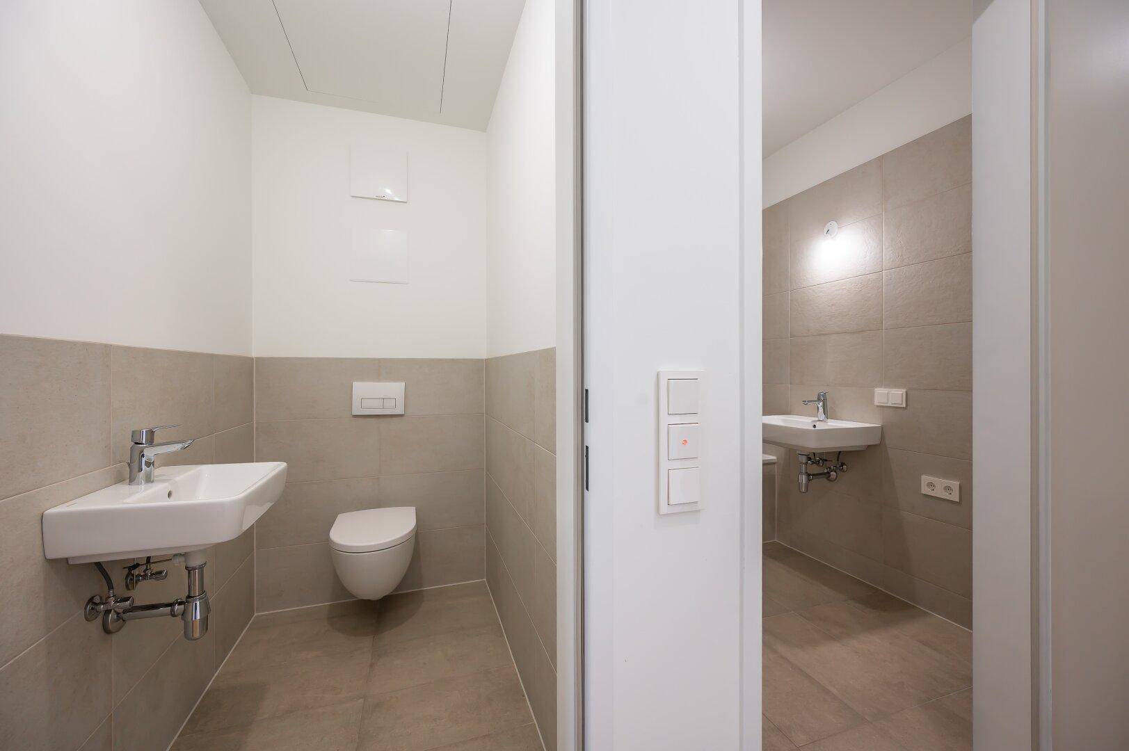 Modernes Gäste-WC mit Wand-WC, Waschbecken und hellen Fliesen.
