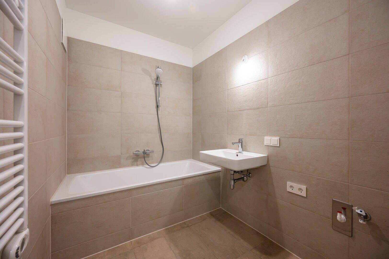 Helles Badezimmer mit Badewanne, Waschbecken und beheiztem Handtuchhalter.