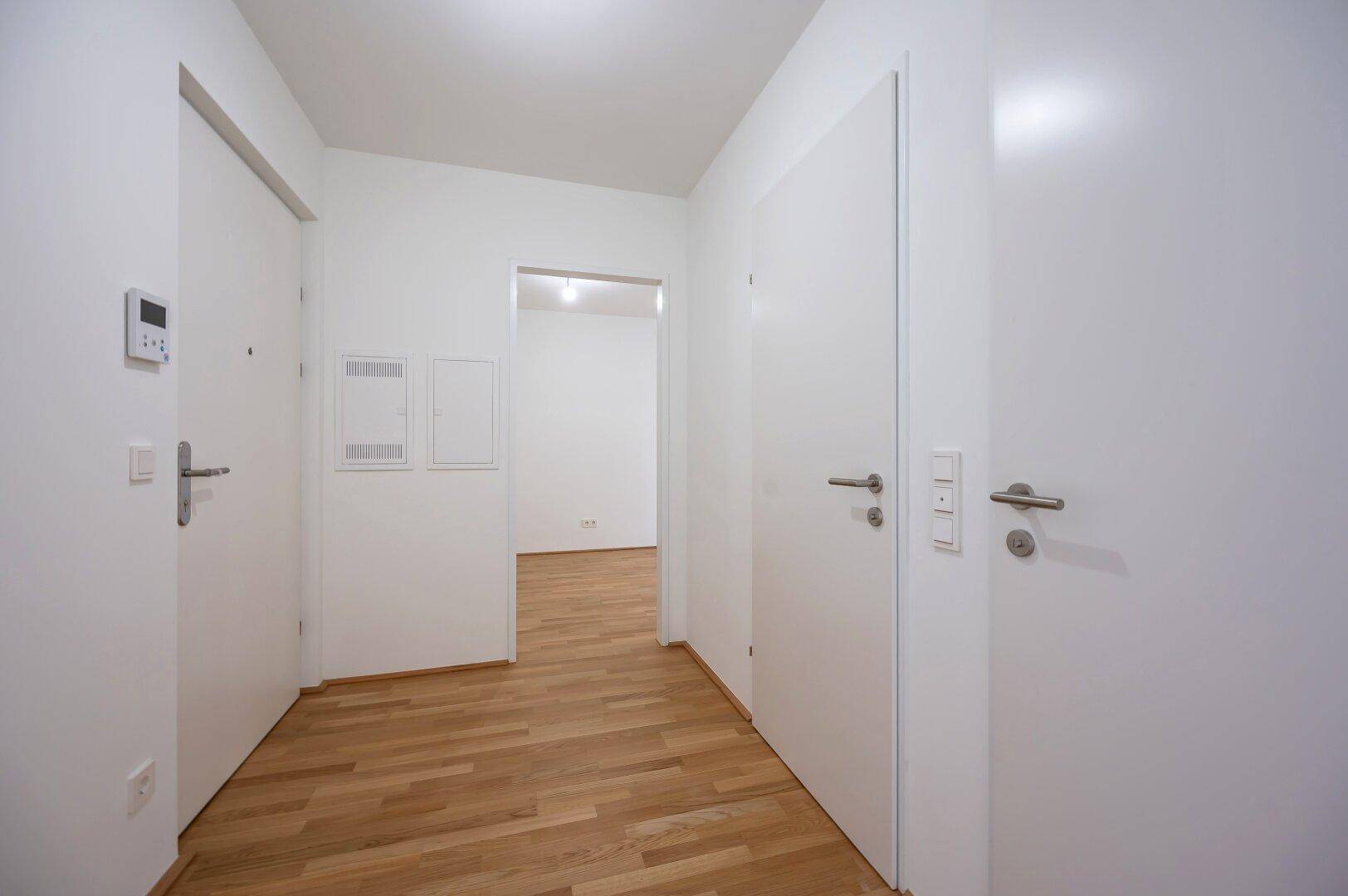 Moderner Flur mit hellen Wänden und Holzboden, verbindet verschiedene Räume der Wohnung.