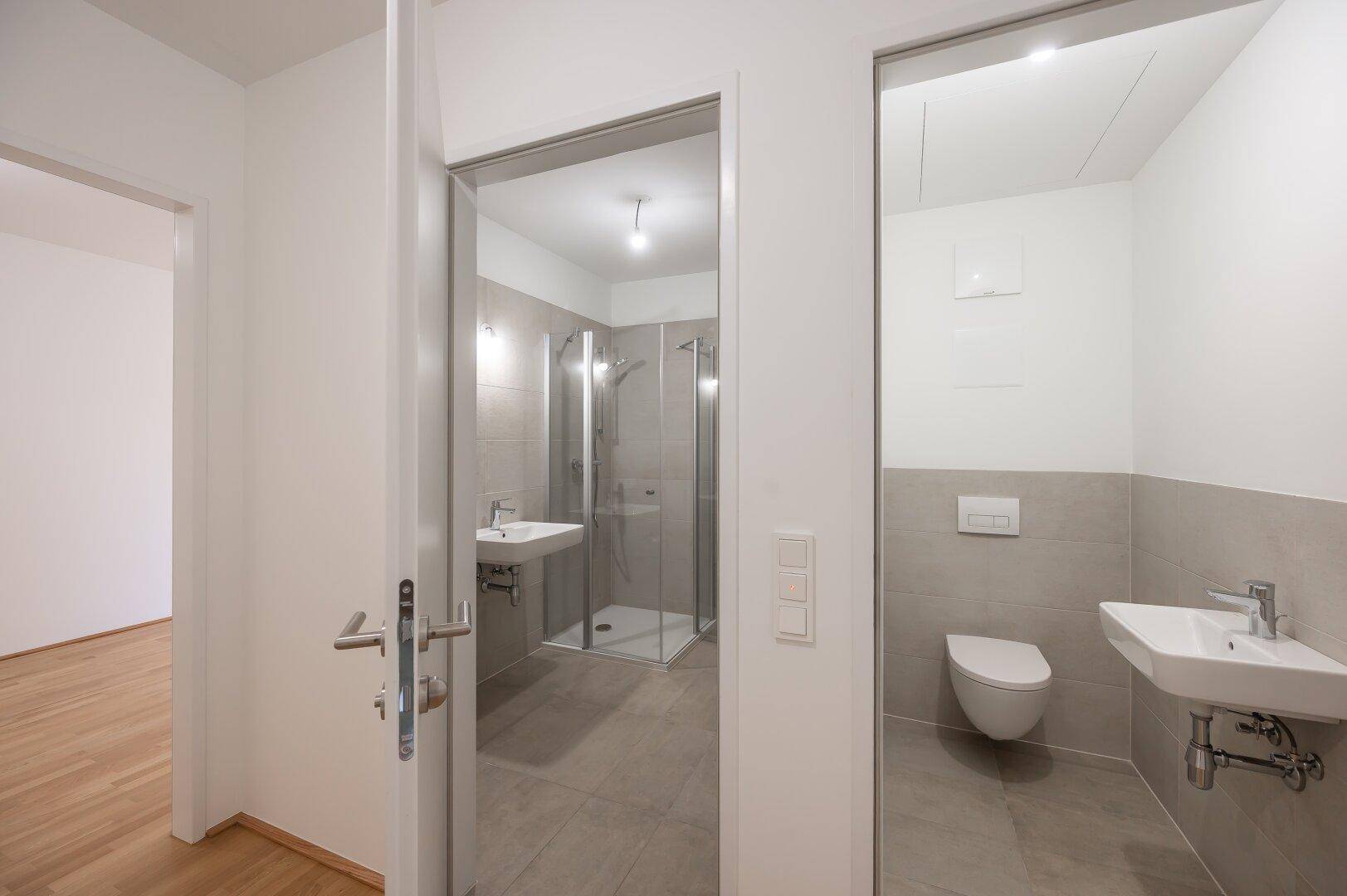 Blick in ein modernes Badezimmer mit Dusche und ein separates Gäste-WC.