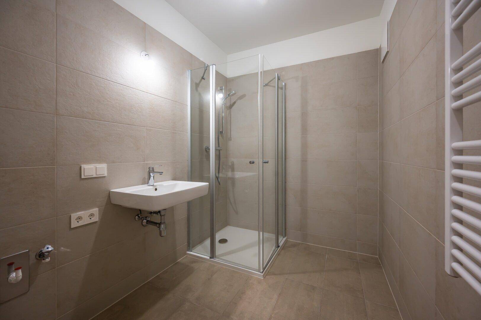 Modernes Badezimmer mit Duschkabine, Waschbecken und beheiztem Handtuchhalter.